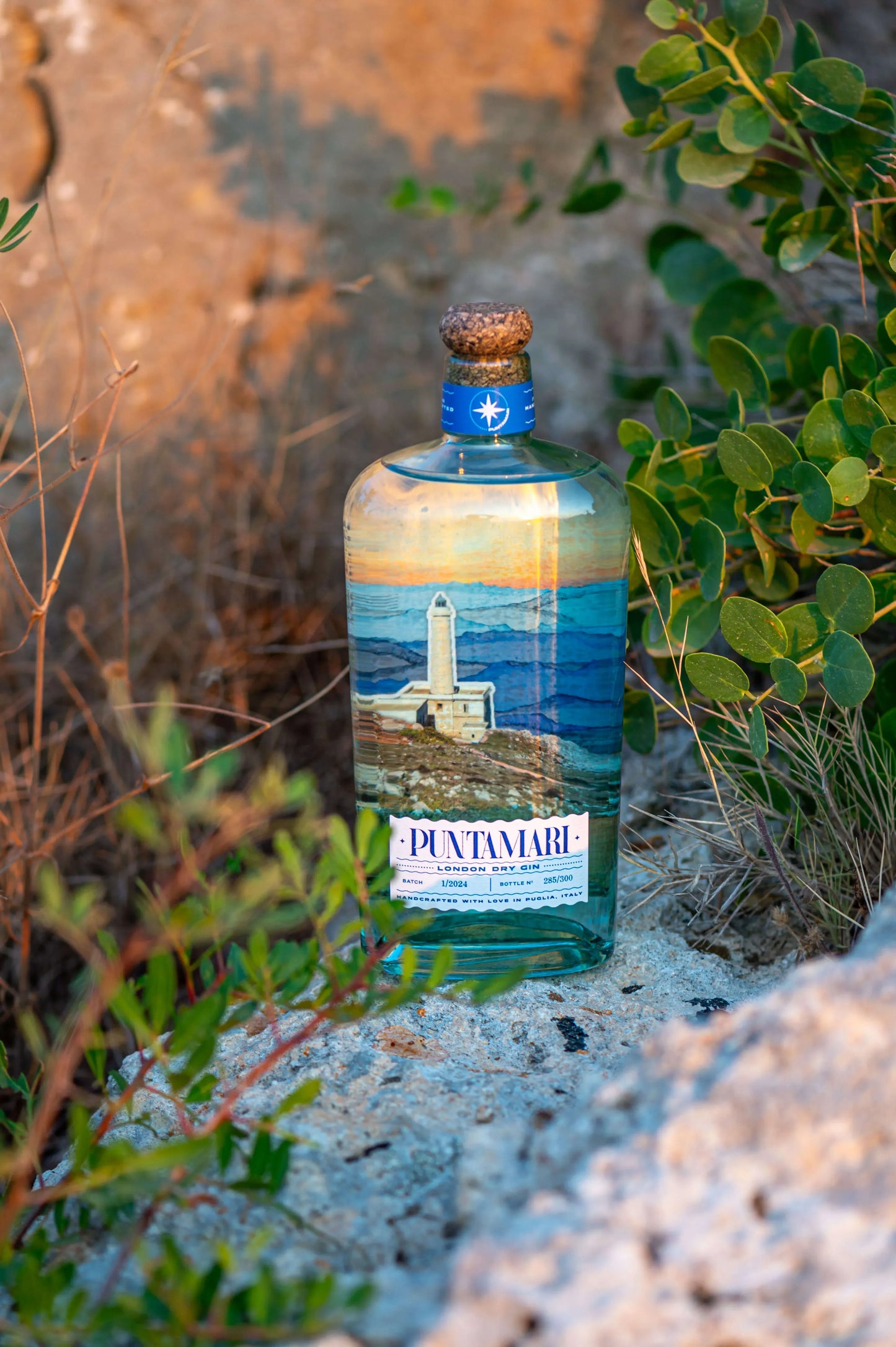 Bottiglia di gin artigianale italiano Puntamari immersa nella macchia mediterranea del Salento all'alba, un autentico gin pugliese