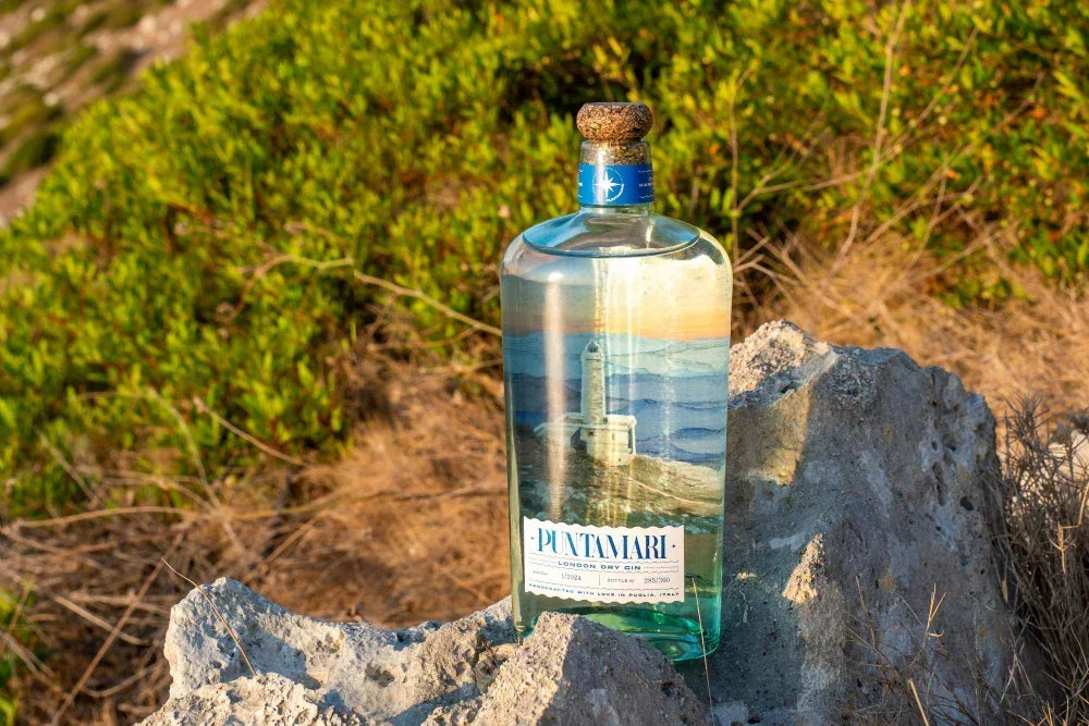 Dettaglio della bottiglia di Puntamari Gin, eccellenza del London Dry italiano prodotto in Puglia, appoggiata sulla roccia della costa salentina
